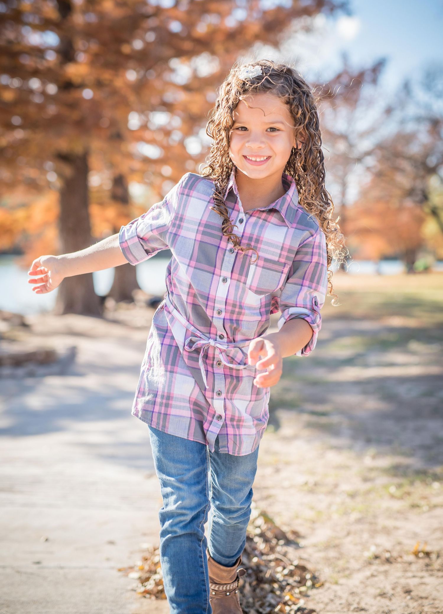 Girl in plaid shirt and jeans playing outside during autumn with orange trees in background during Omaha photography session.