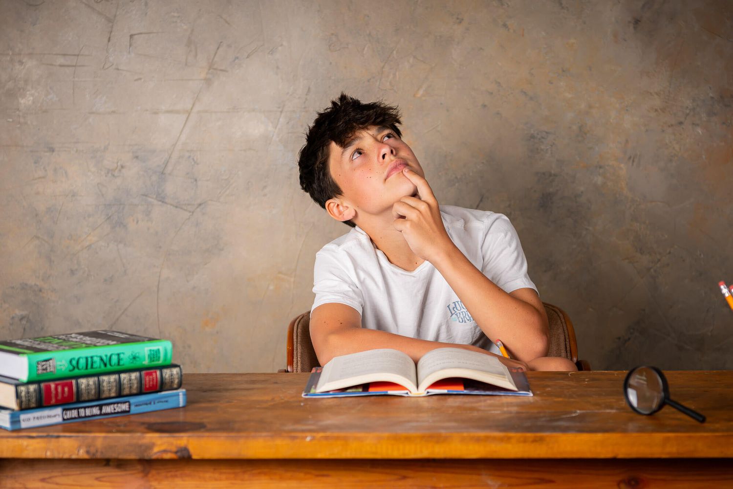 Student sitting at wooden desk daydreaming while studying with textbooks and school supplies.
