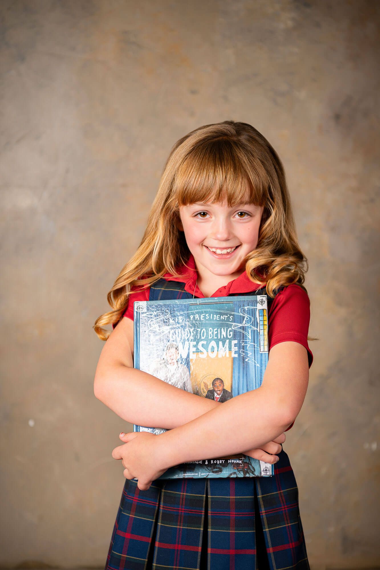 A student in school uniform holding educational books against a textured background.