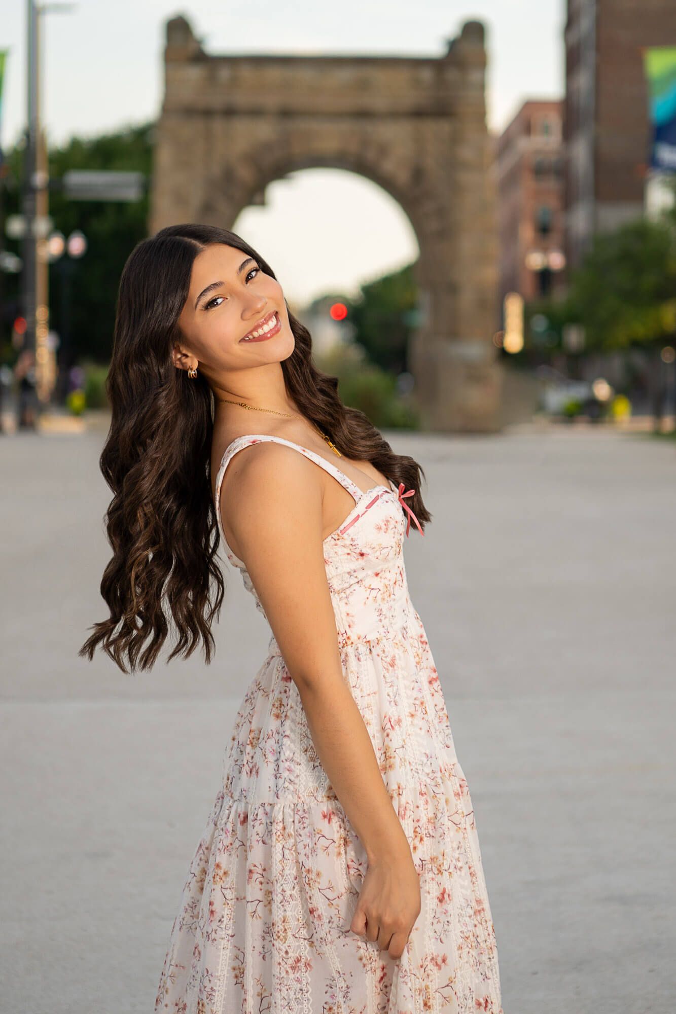 A joyful twirl in a floral summer dress on a city street with urban architecture in the background.