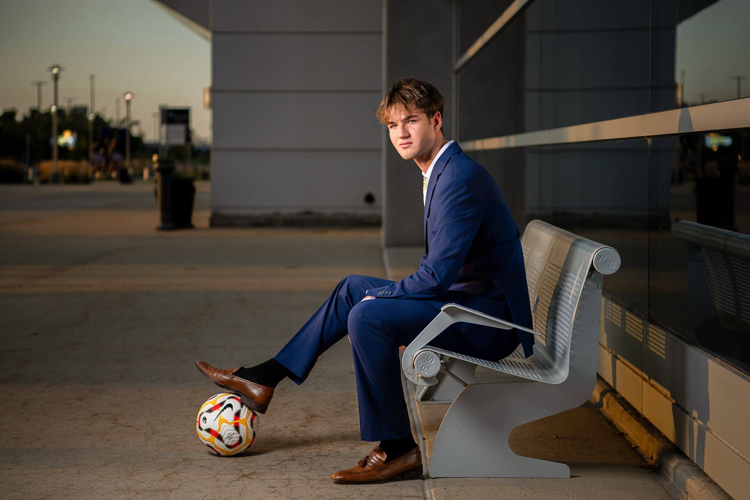 A person in a blue suit sits on a white bench while scrolling through a smartphone device.