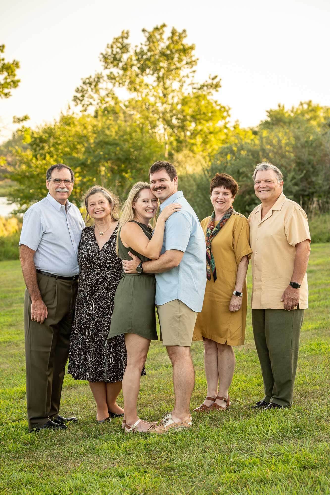A group poses together on a grassy hill during golden hour, creating a cheerful family portrait.