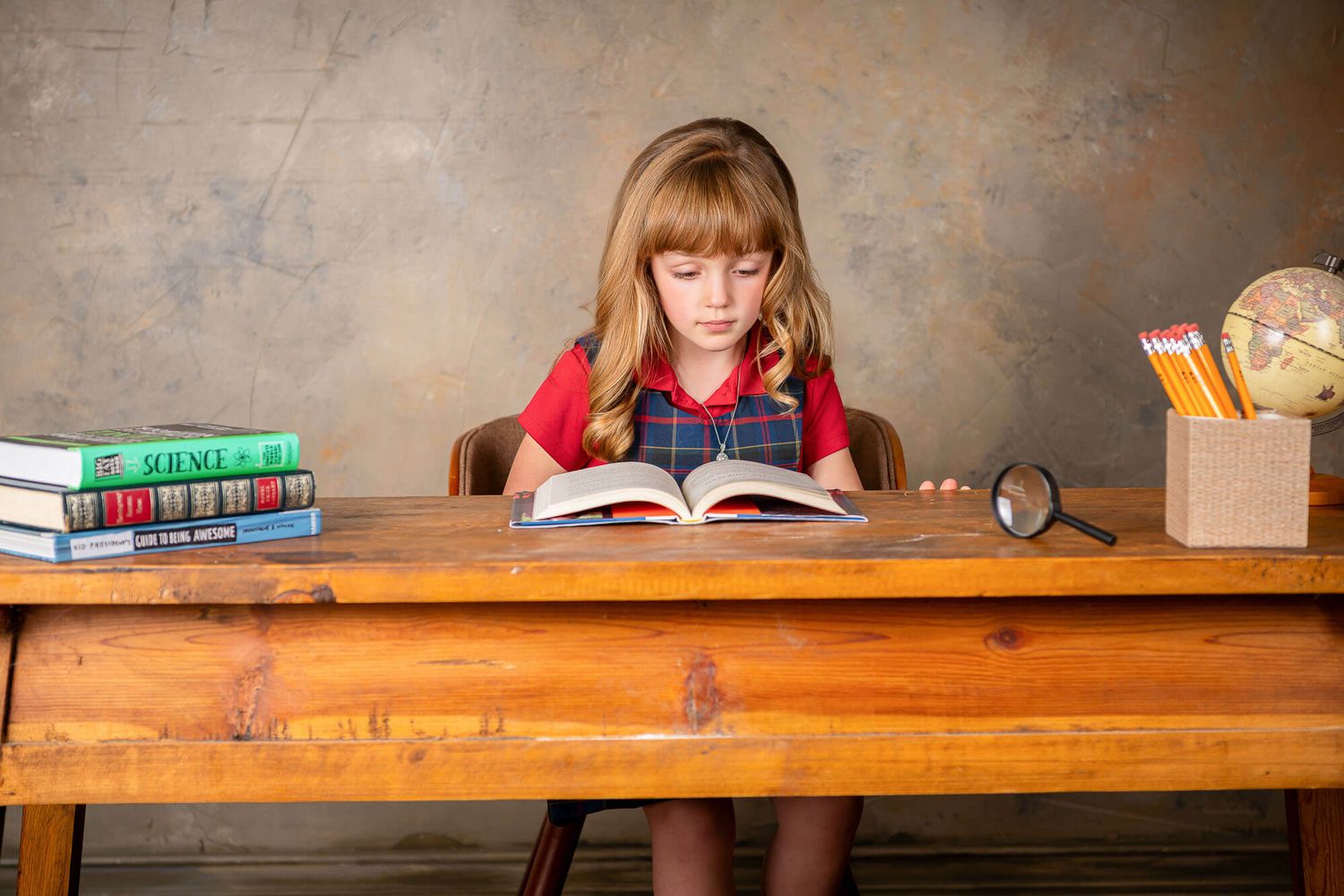 Student writing at wooden desk with textbooks and school supplies in classroom setting.