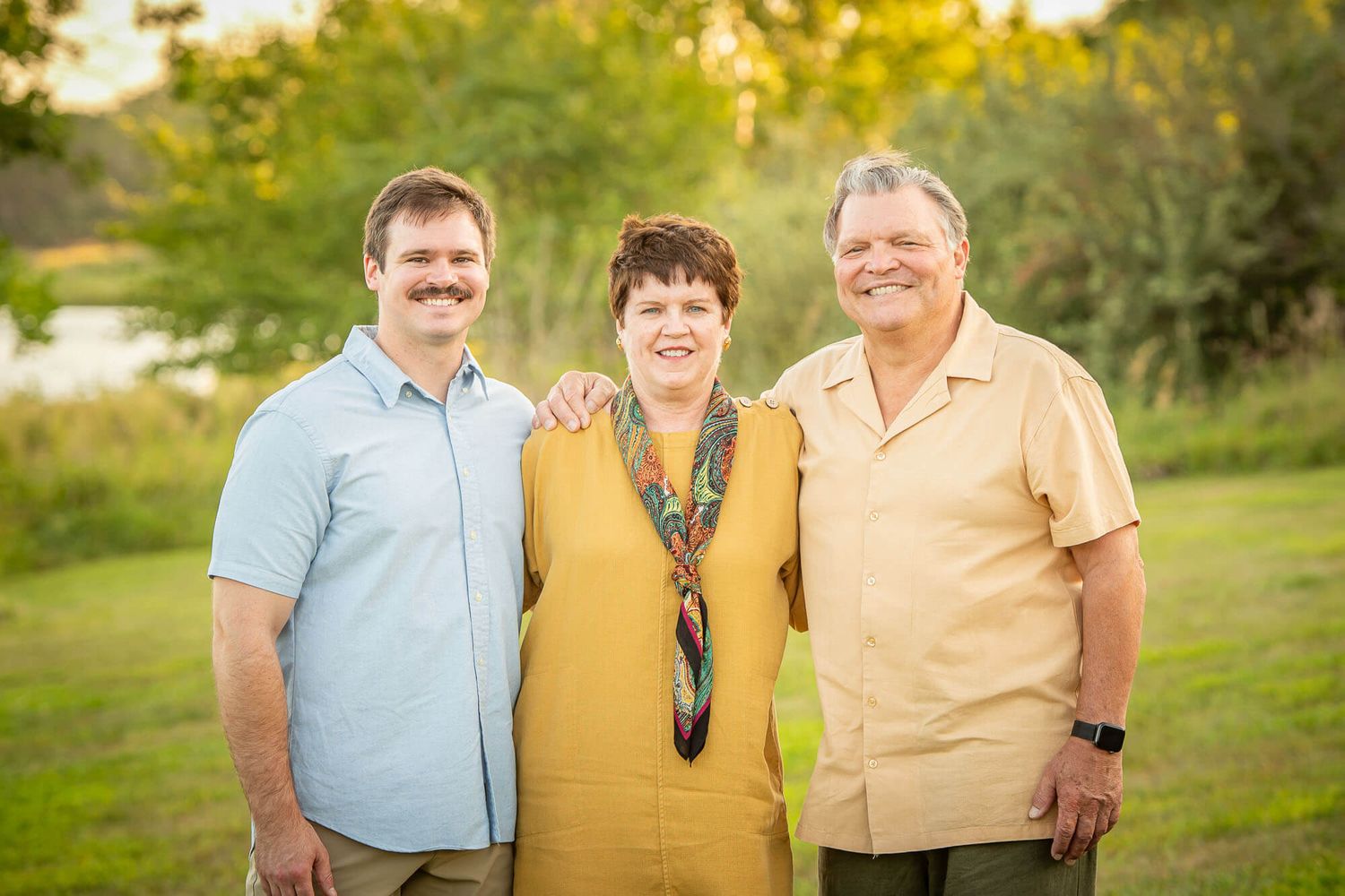 Three people stand together outdoors in a grassy field during golden hour sunset lighting.