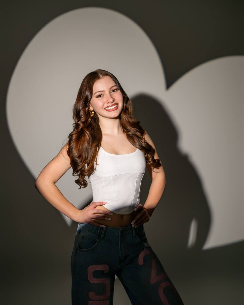 Omaha senior from Northwest High School in white top and jeans with a heart shaped light behind her at Studio 108