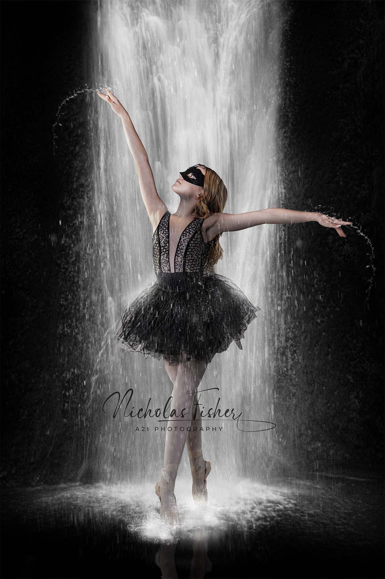 A ballerina in a black tutu performs an elegant dance pose under a cascading waterfall in dramatic lighting.