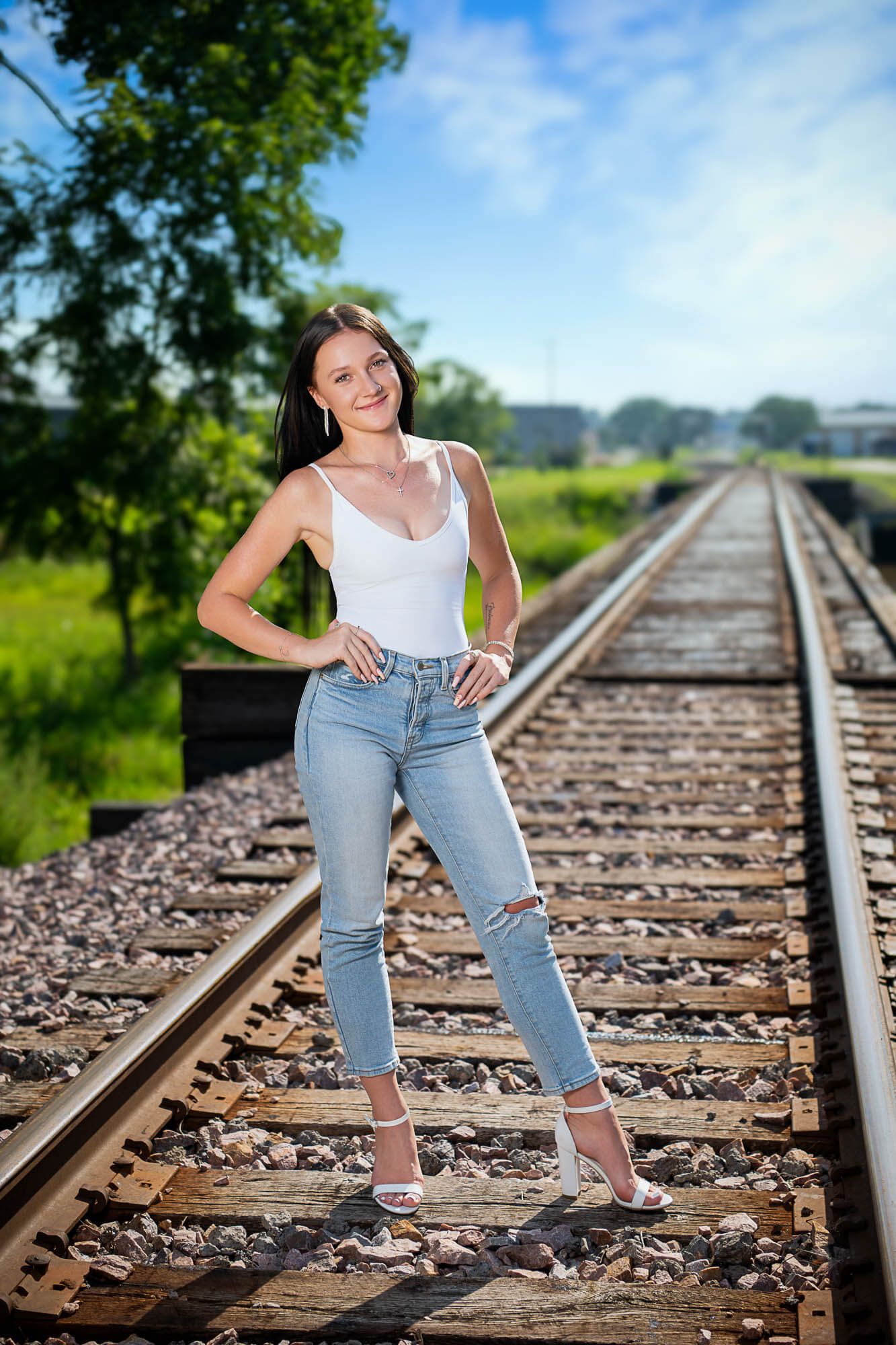 A series of photos taken on railroad tracks with someone posing in jeans and a white tank top on a sunny day.