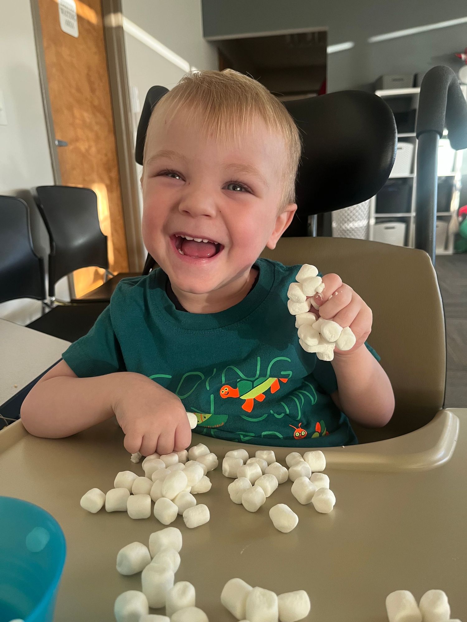 A person wearing a green t-shirt sits in a high chair while playing with white cotton balls or marshmallows.