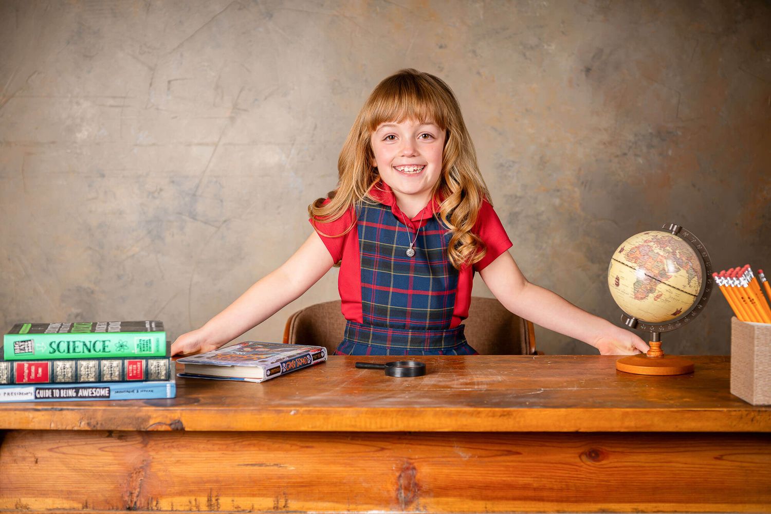 Student sits at wooden desk with globe and books in educational setting showing learning environment.