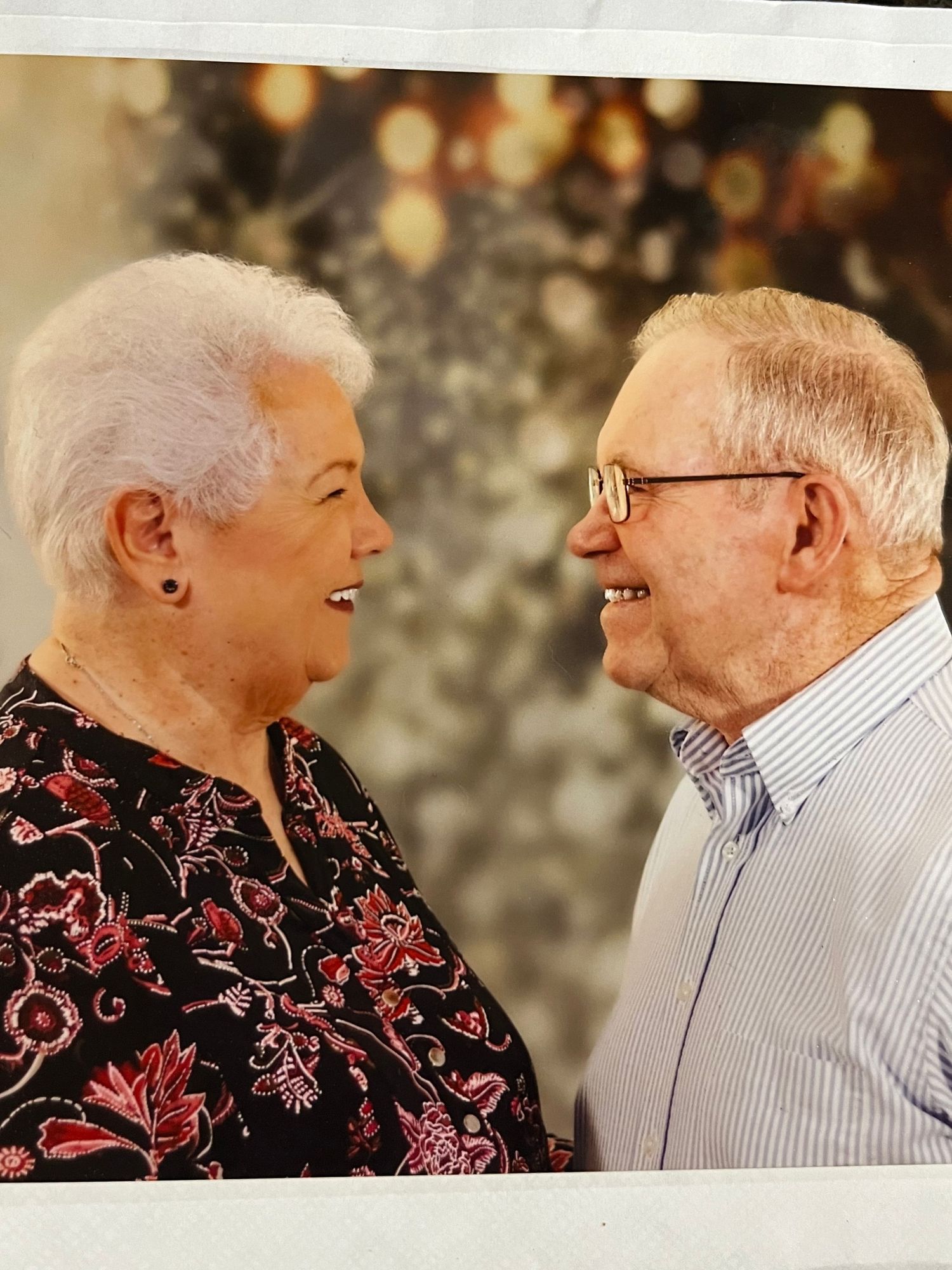 An elderly couple shares a joyful moment together while wearing casual attire against a sparkly backdrop.