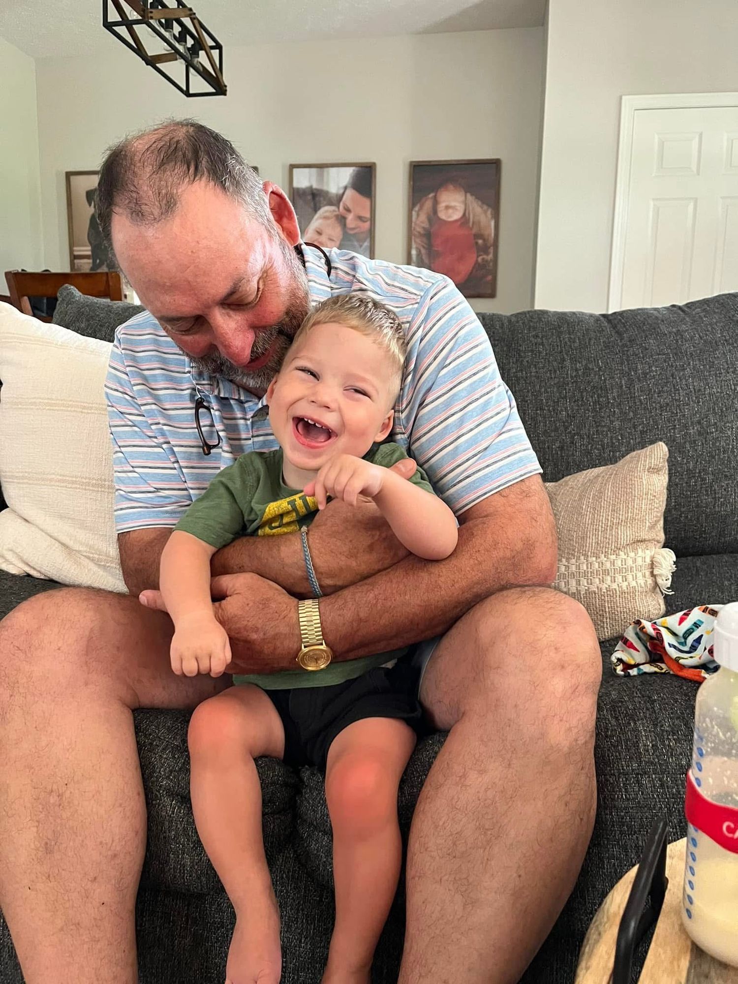 A person in a striped shirt shares a joyful moment with a laughing young child on a gray couch.