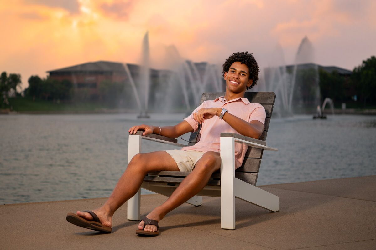 Senior photography of black male at Heartland of America Park in Omaha sitting in a chair with the fountain in the background