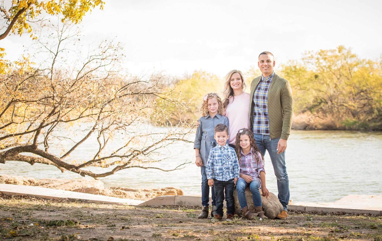 Family enjoying a golden autumn sunset together at the beach with fall foliage in the background.