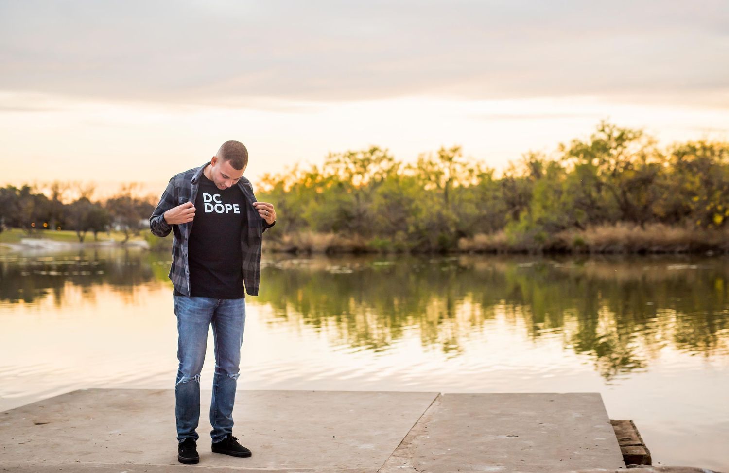 A person stands by a serene lake at sunset with golden light reflecting on the calm water during Omaha family photography session.