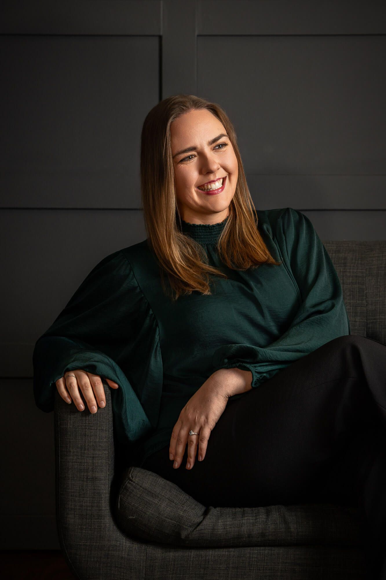 Artistic portrait of someone in dark clothing lounging on a couch in moody lighting.