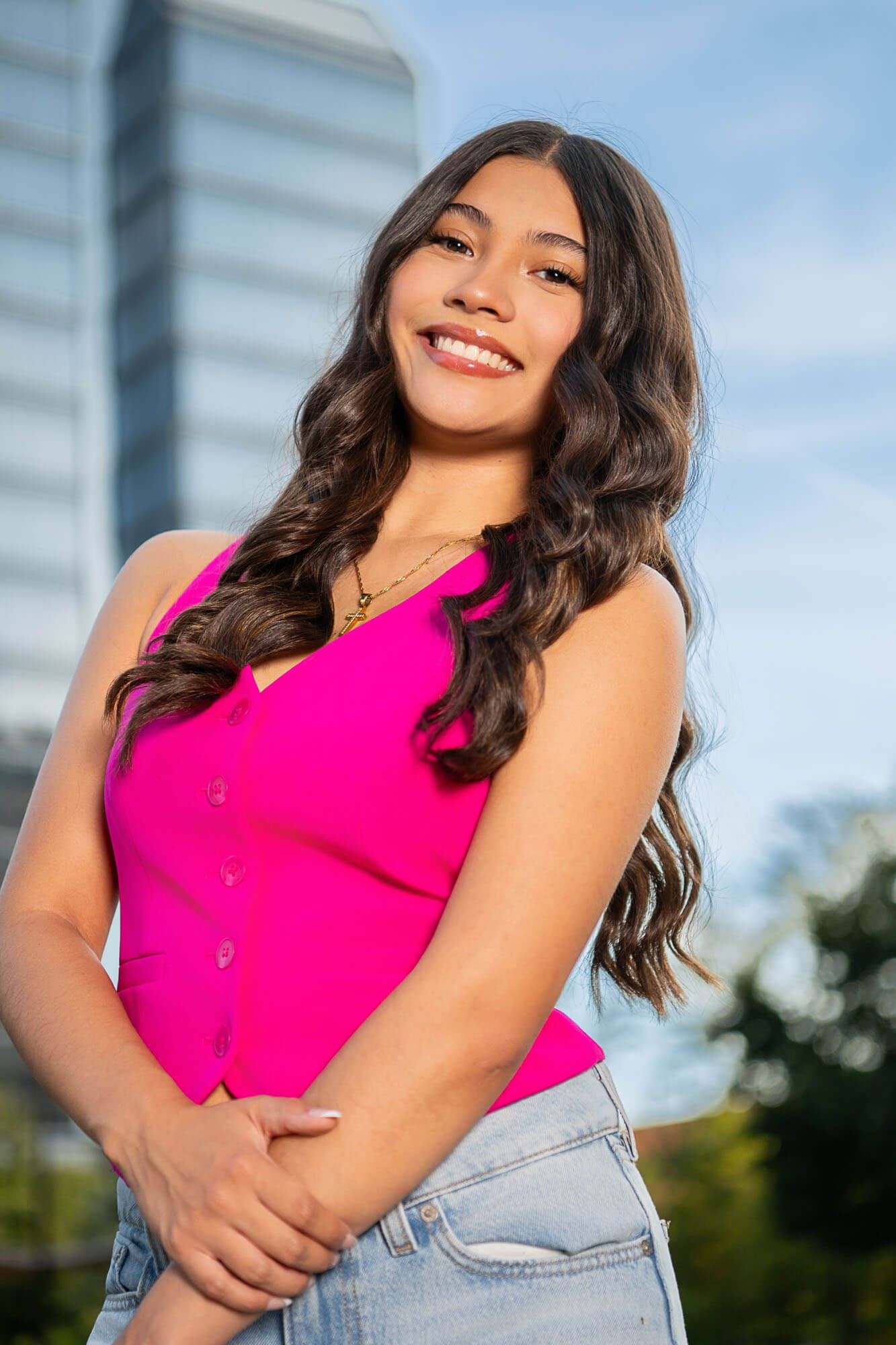 A person in a bright pink sleeveless top and light denim jeans poses outdoors during golden hour.
