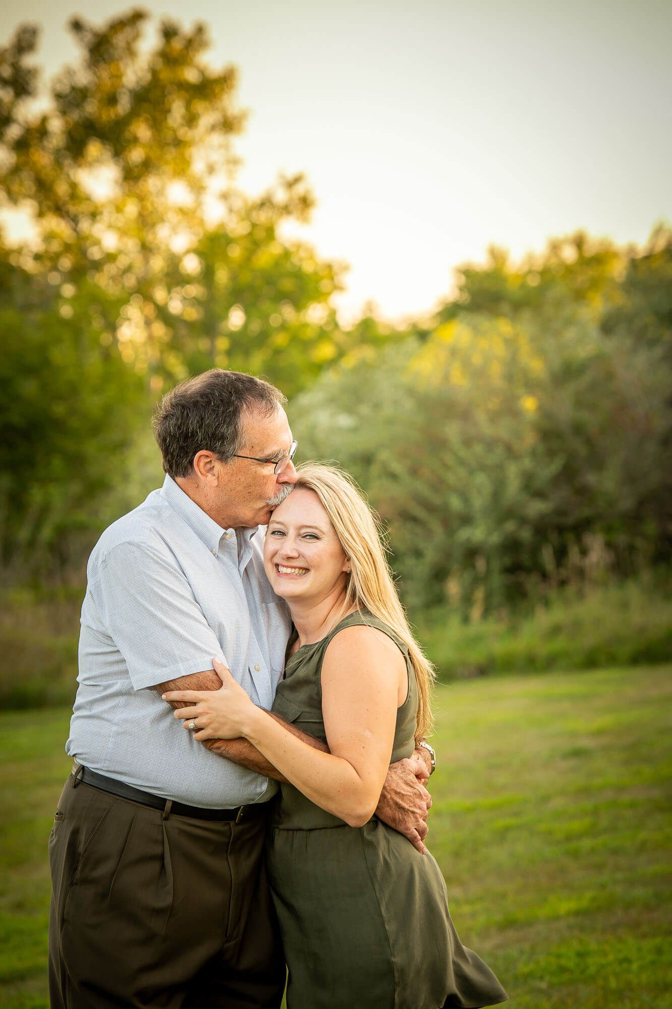 Two people share an affectionate moment while laughing together in a sunlit outdoor setting.