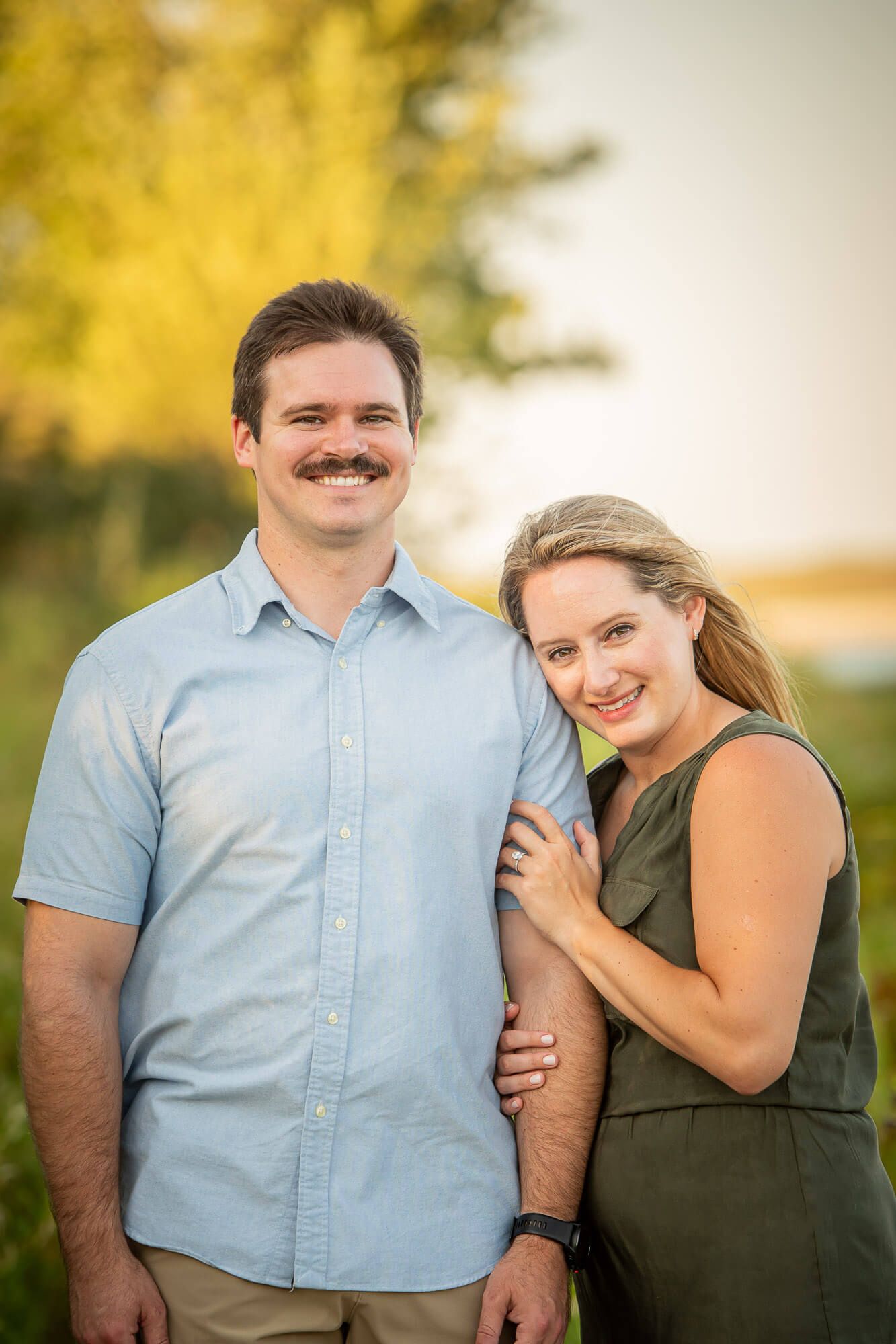 A couple poses together outdoors during a sunset photoshoot with warm golden lighting and natural scenery.