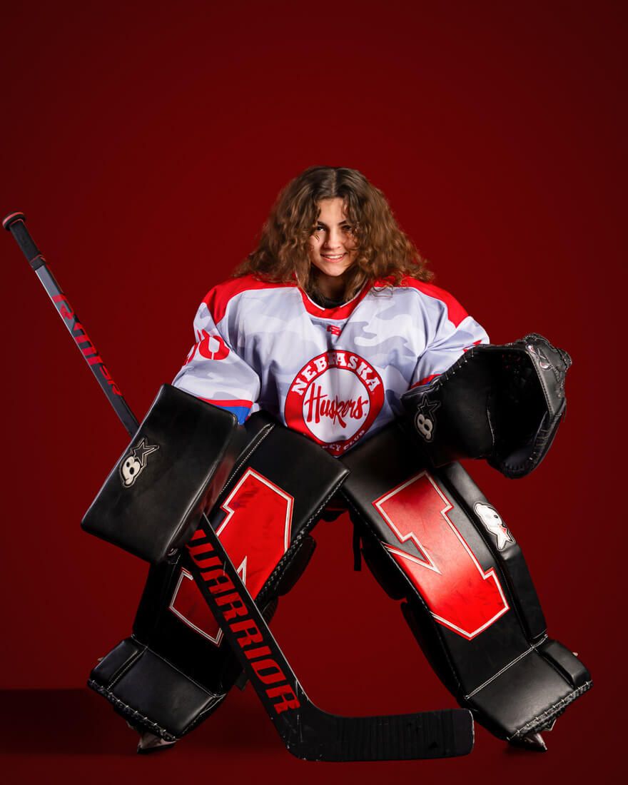 A hockey goalie in red and white jersey performs a sliding save sequence against a dark red background.