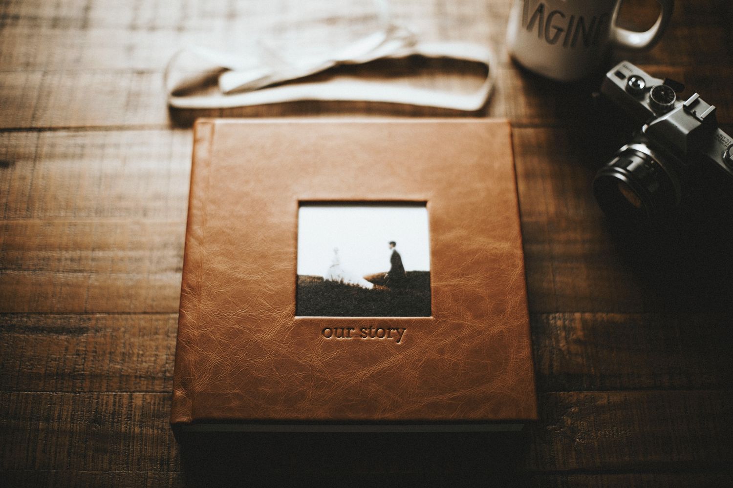 A leather photo album with a small photograph and vintage camera on wooden table, captured in warm brown tones.