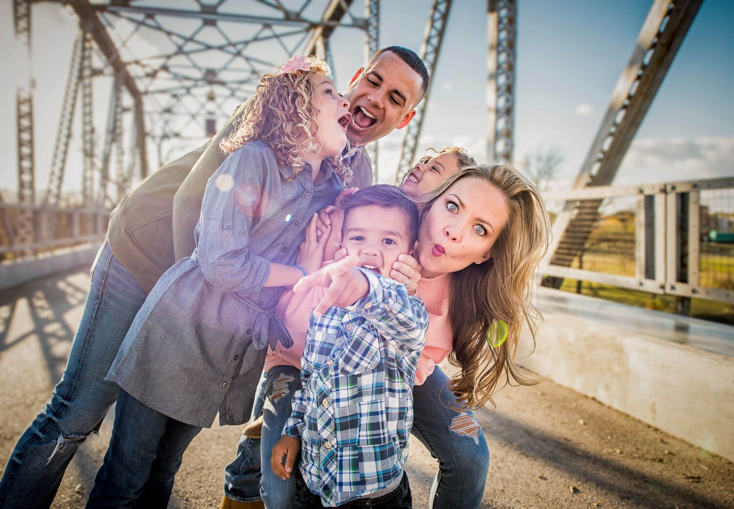 Happy couple poses playfully together on a bridge during a sunny outdoor engagement photoshoot.