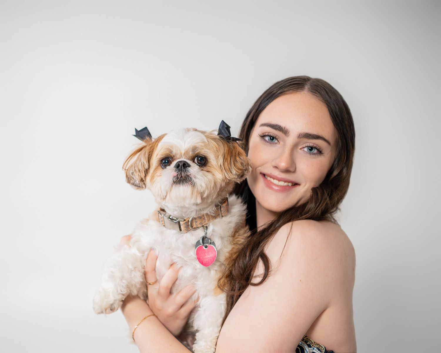 A person in black holds a small Shih Tzu dog against a light gray studio background.