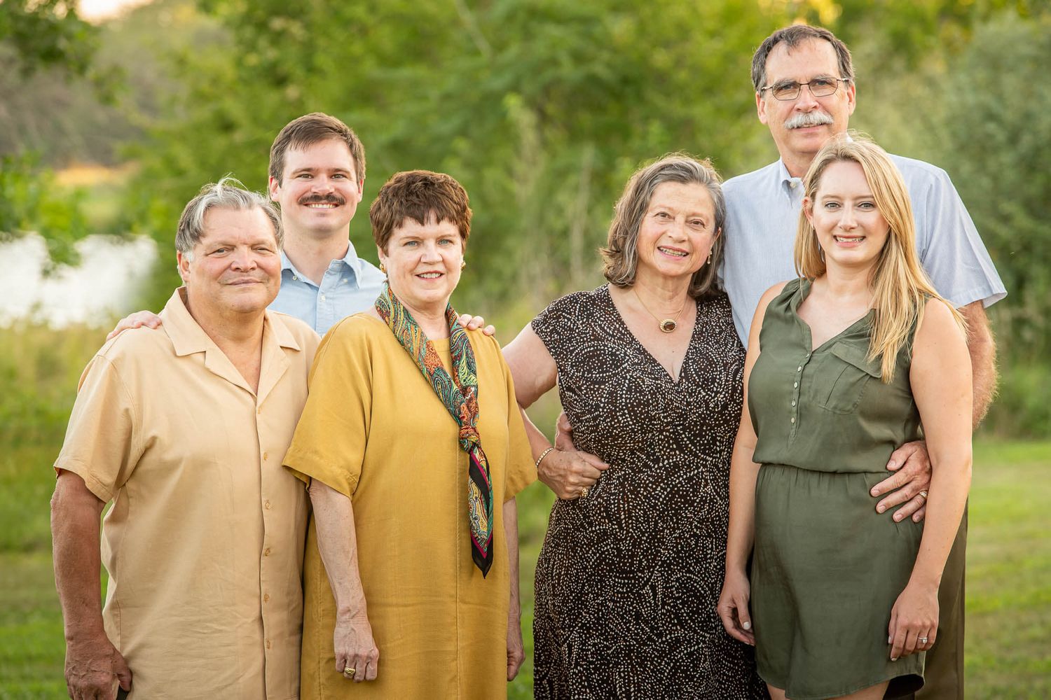 A multi-generational family group poses together outdoors wearing coordinated casual attire in warm earth tones.