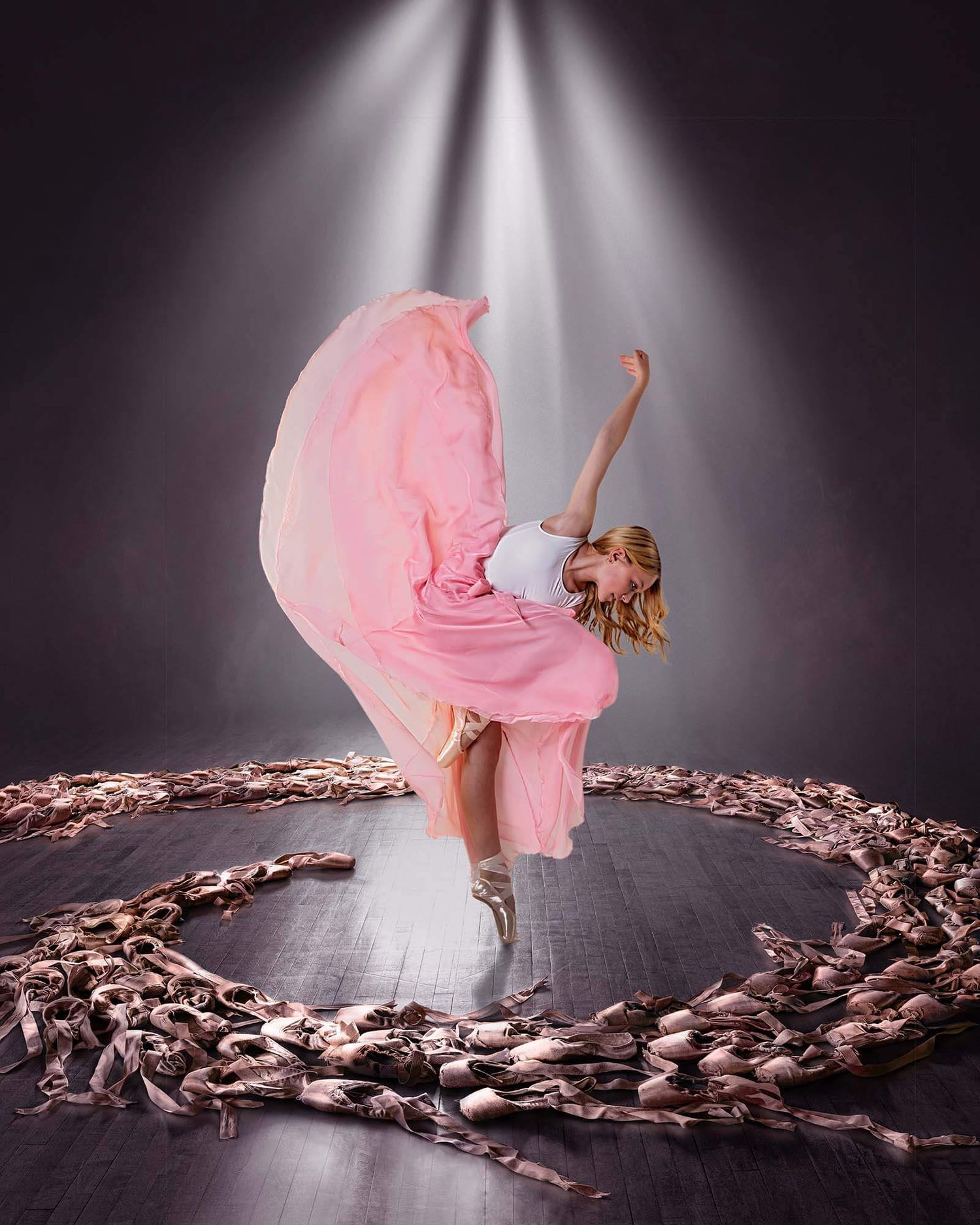 A flowing pink dress twirls gracefully through scattered rose petals on a dark stage with dramatic lighting.