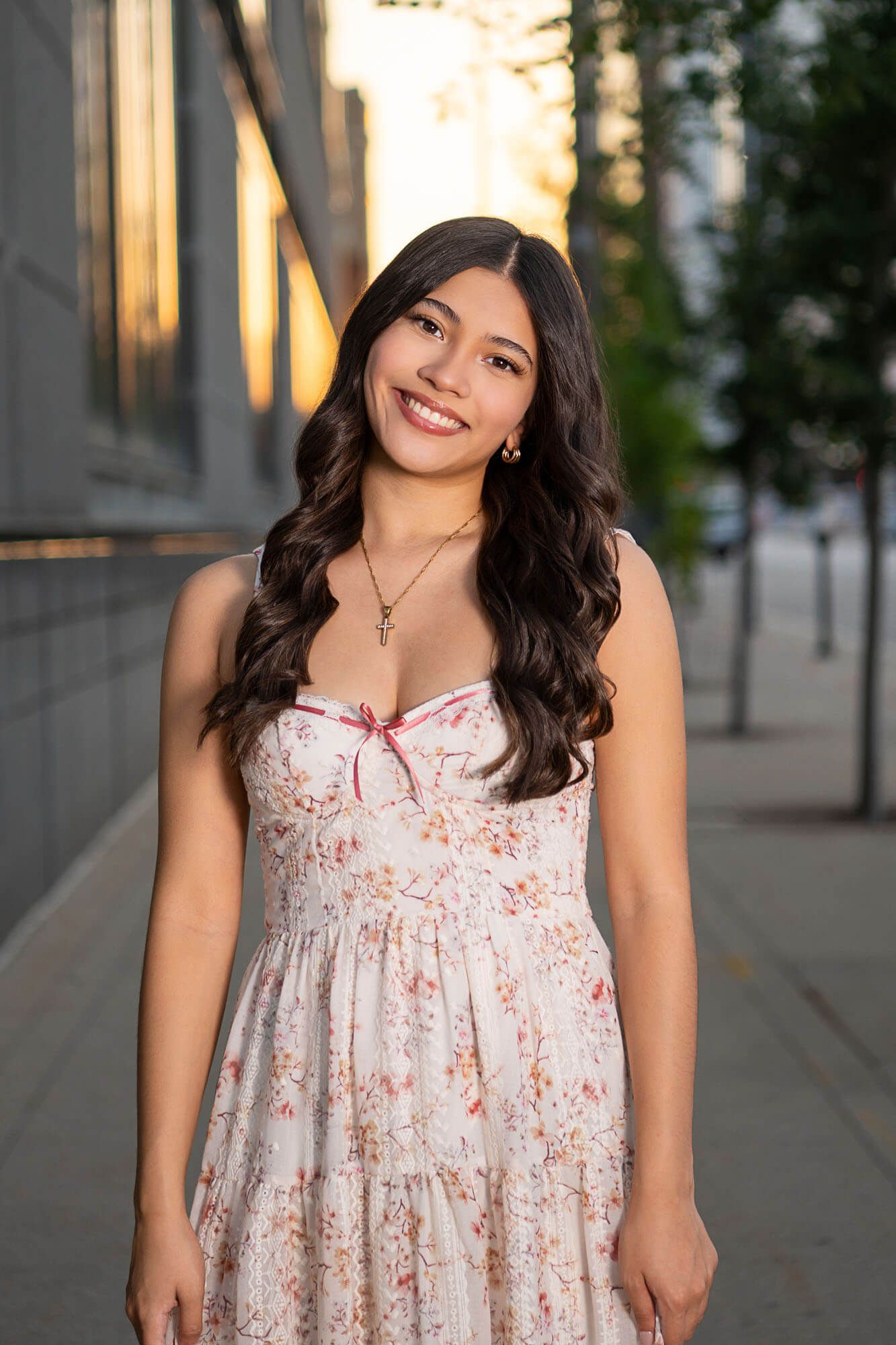 A person wearing a floral white sundress poses in an urban setting with modern architecture in the background.
