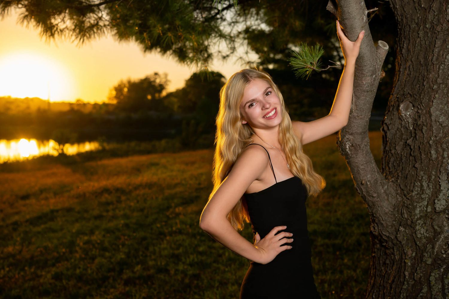 A graduation photo session at sunset shows a graduate in a black dress posing by a tree in golden light.