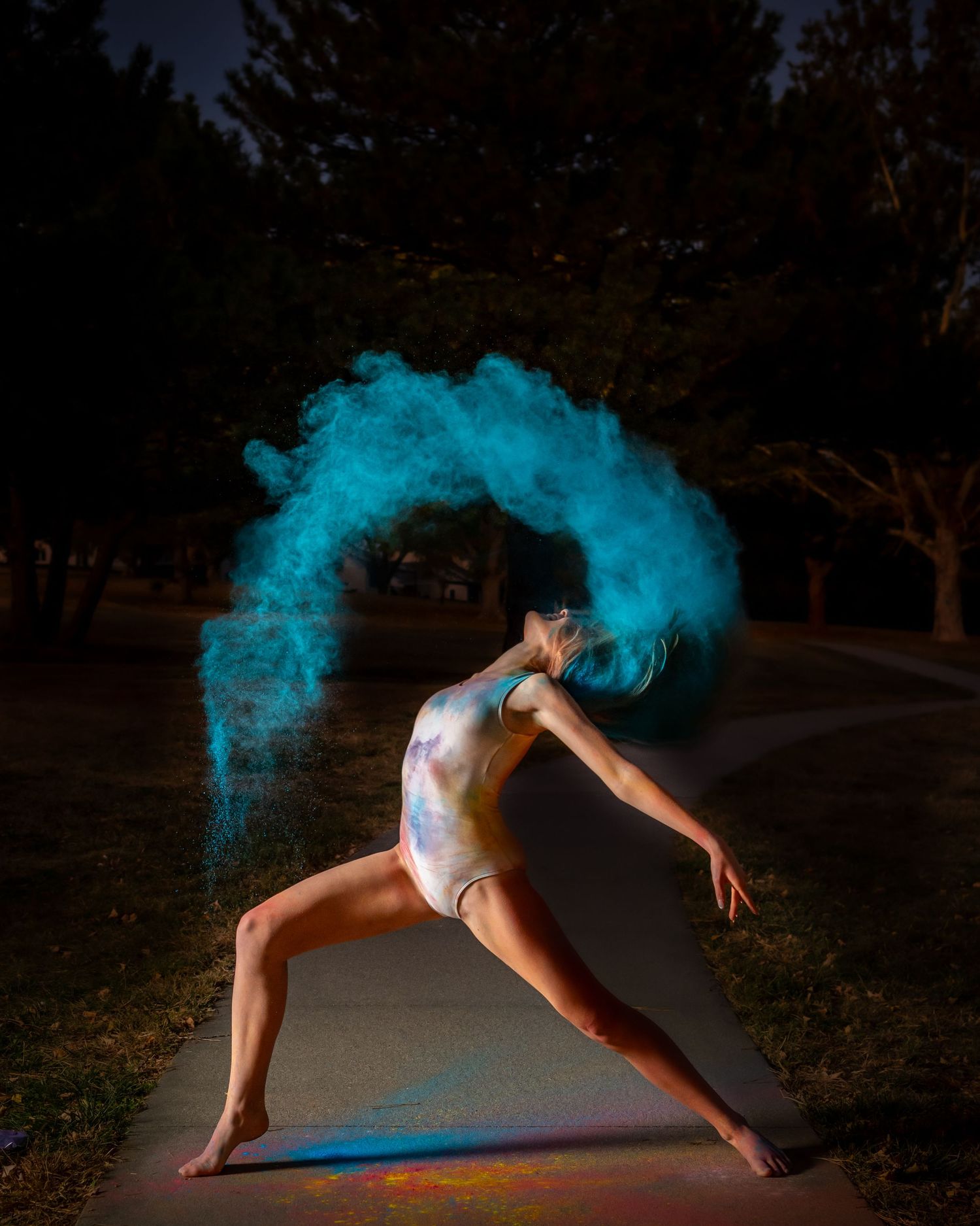 Senior Photographer in Omaha - Dynamic dance pose illuminated by vibrant blue powder explosion effect in a dark nighttime outdoor setting.