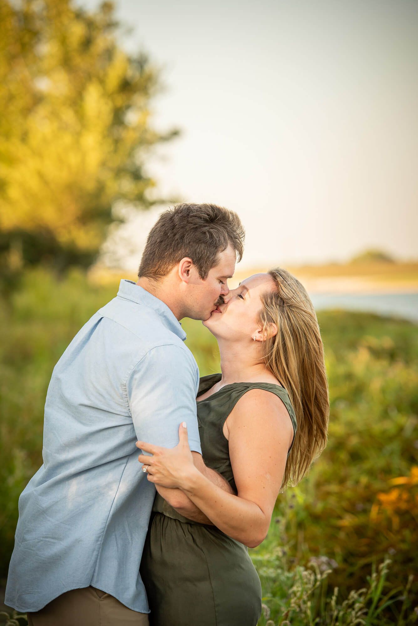 Romantic couple embracing in a sunlit meadow during golden hour, dressed in blue and black casual attire.