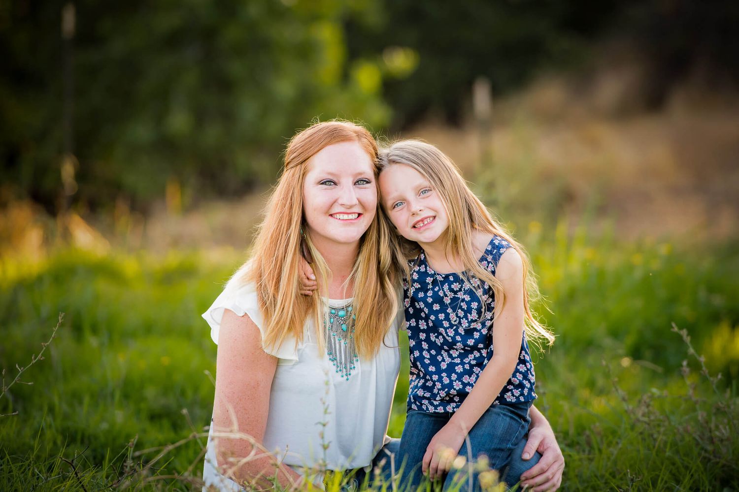 Two friends share joyful moments together while sitting in a sunny meadow filled with wildflowers.