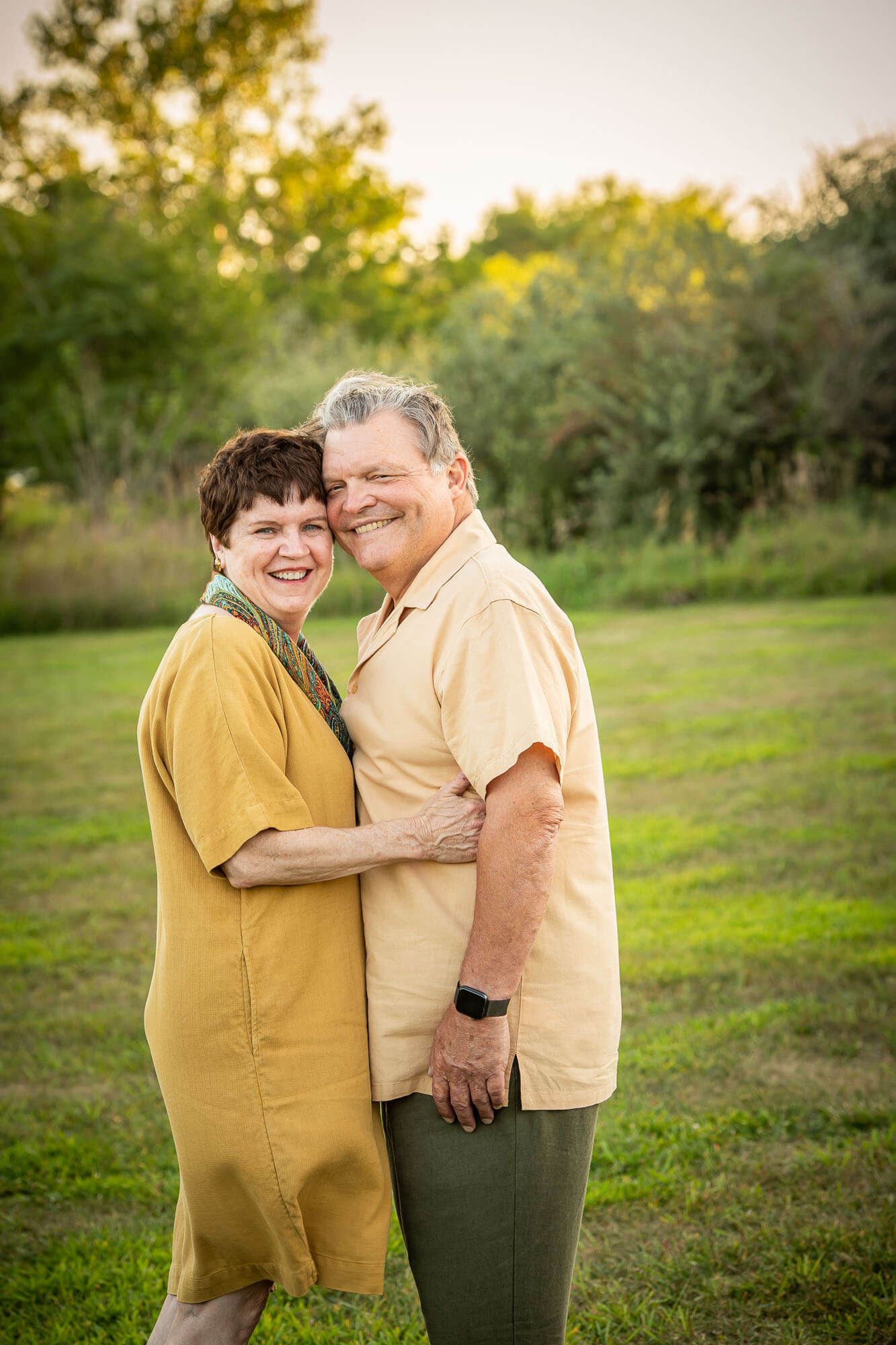 Affectionate couple sharing tender moments in a grassy field at sunset wearing yellow and beige clothing.
