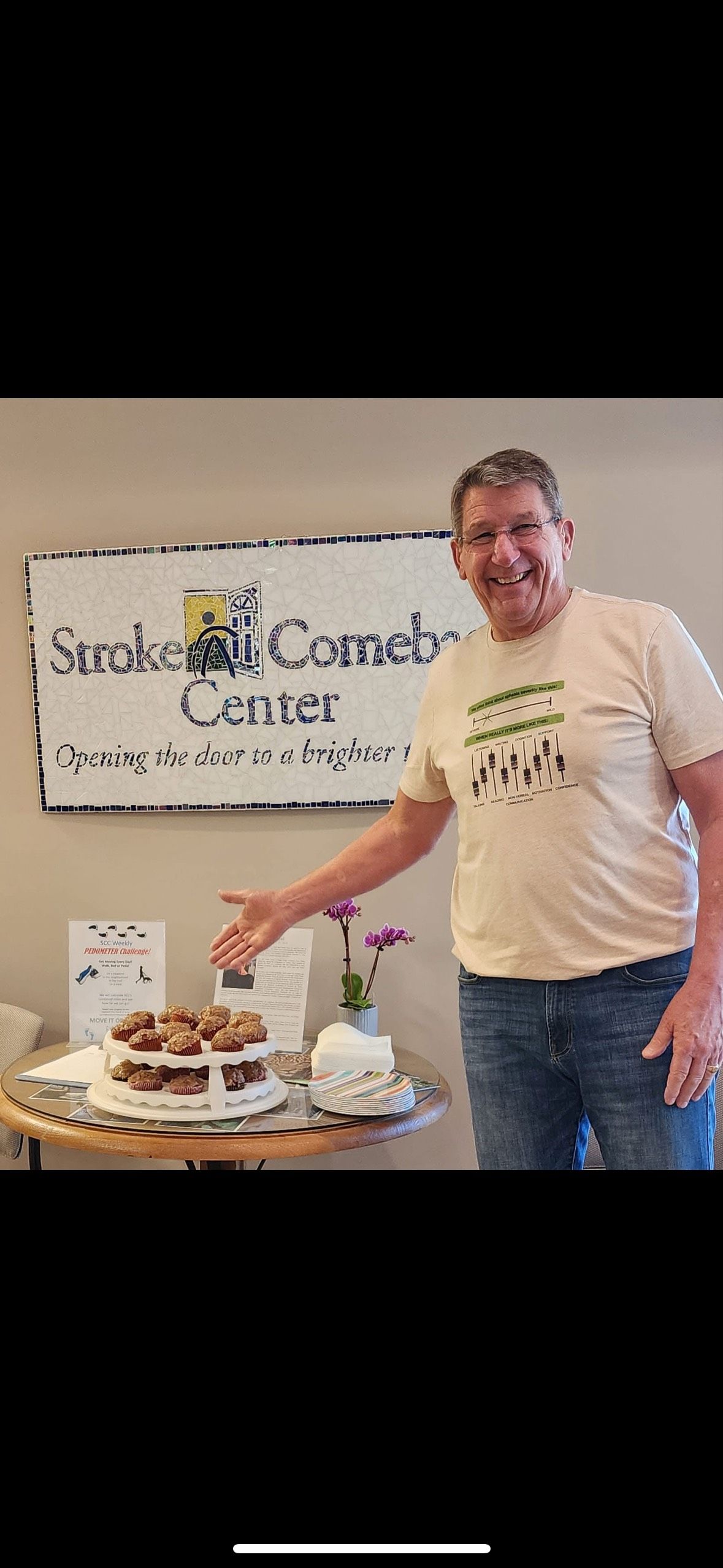 Someone gestures toward a table with treats in front of a Stroke and Comeback Center sign.