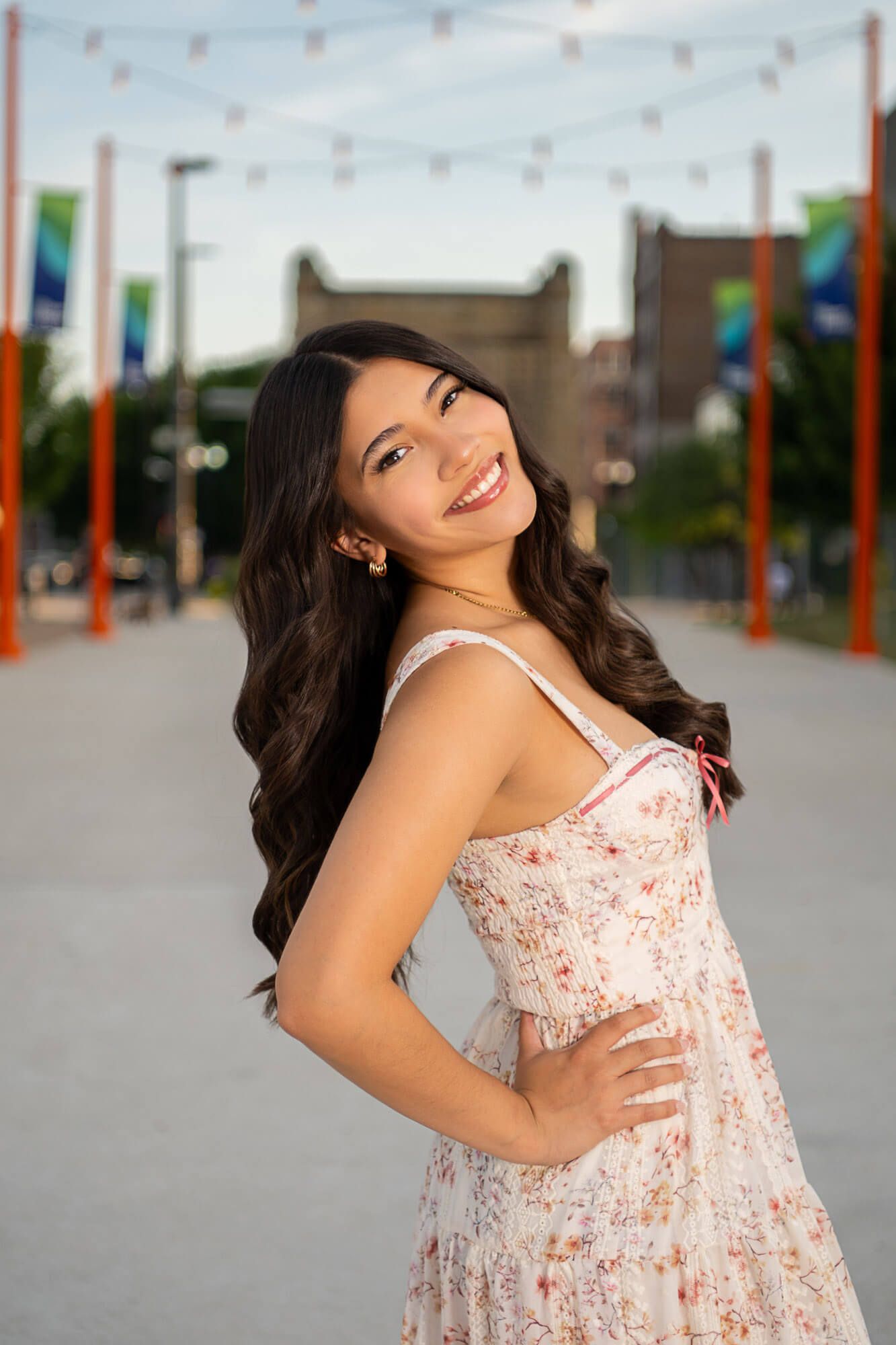 A woman in a floral summer dress poses outdoors with colorful banners in the background.