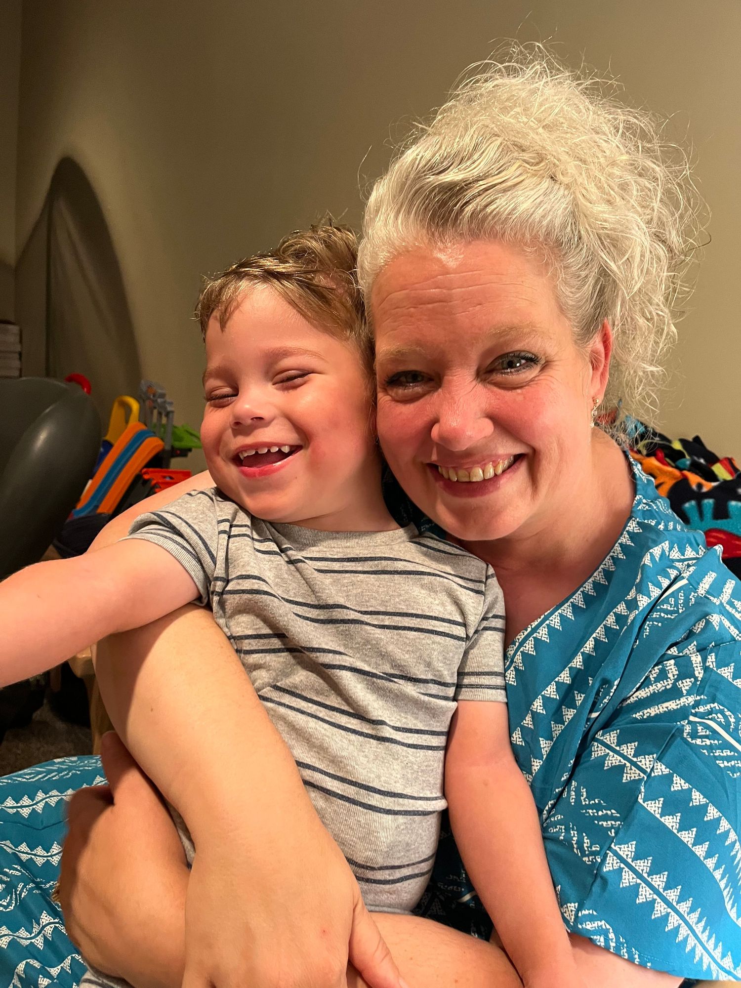 A happy moment shared between a person wearing a blue patterned top and a child in a striped gray shirt.