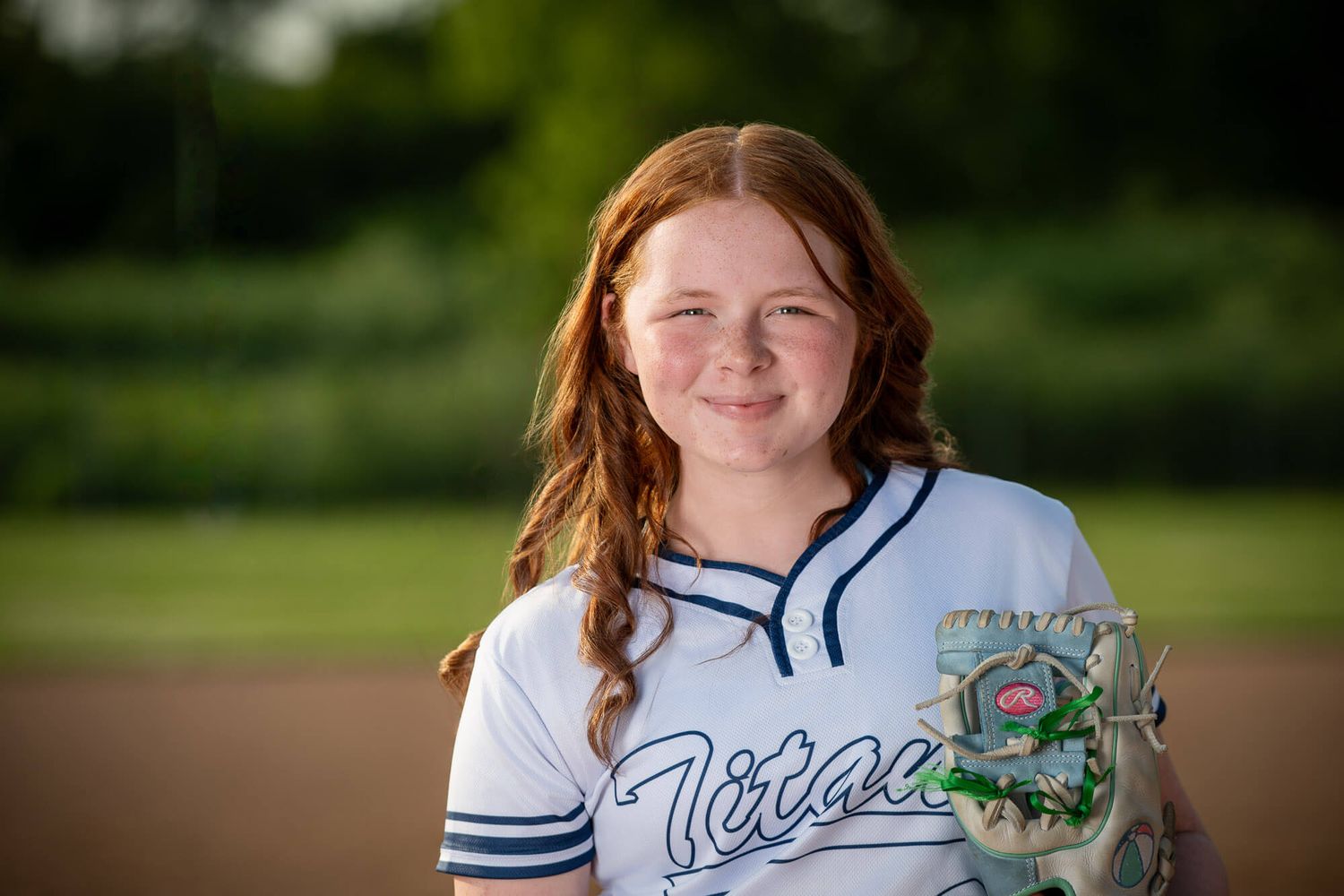 Young girl in Titans softball jersey smiling outdoors, holding glove on a sunny green field.
