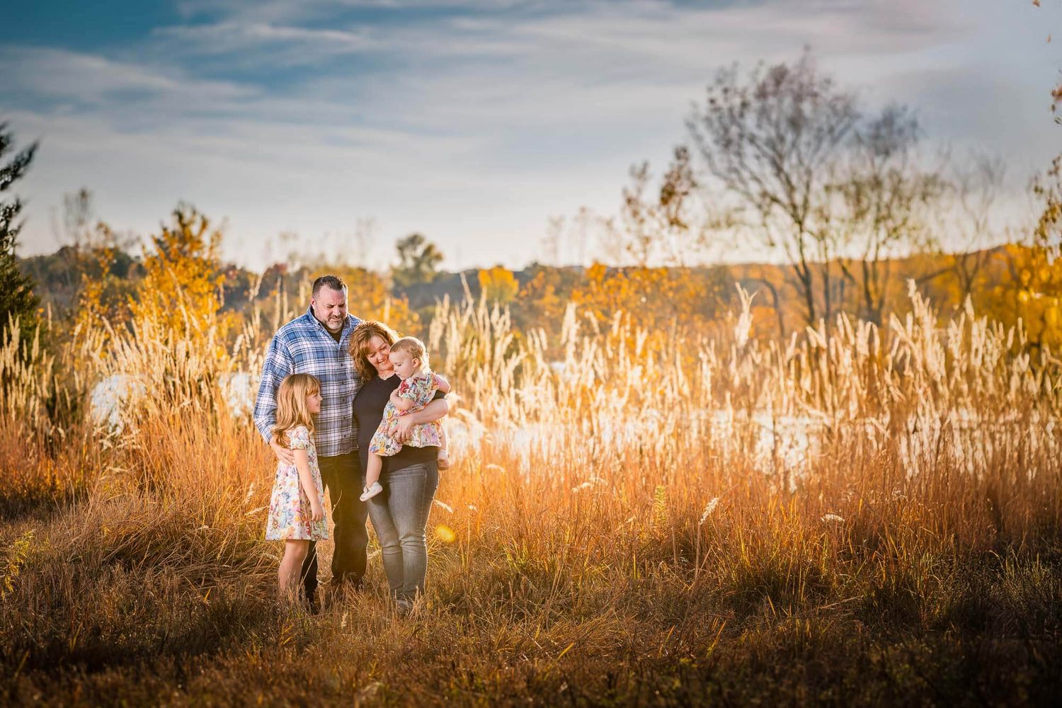 A couple walks together through tall golden grass at sunset in a rustic outdoor setting.