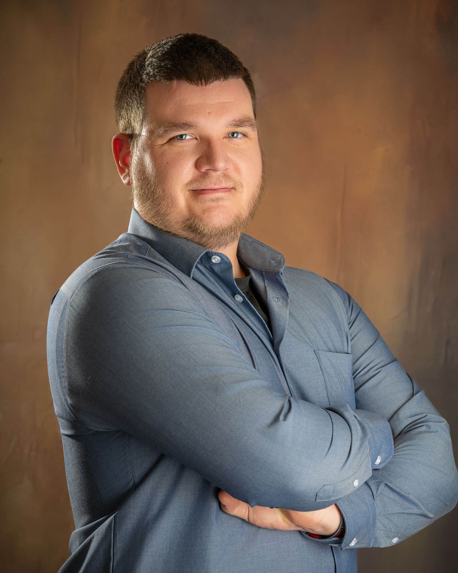 Relaxed business portraits of person in blue shirt posing against brown backdrop.