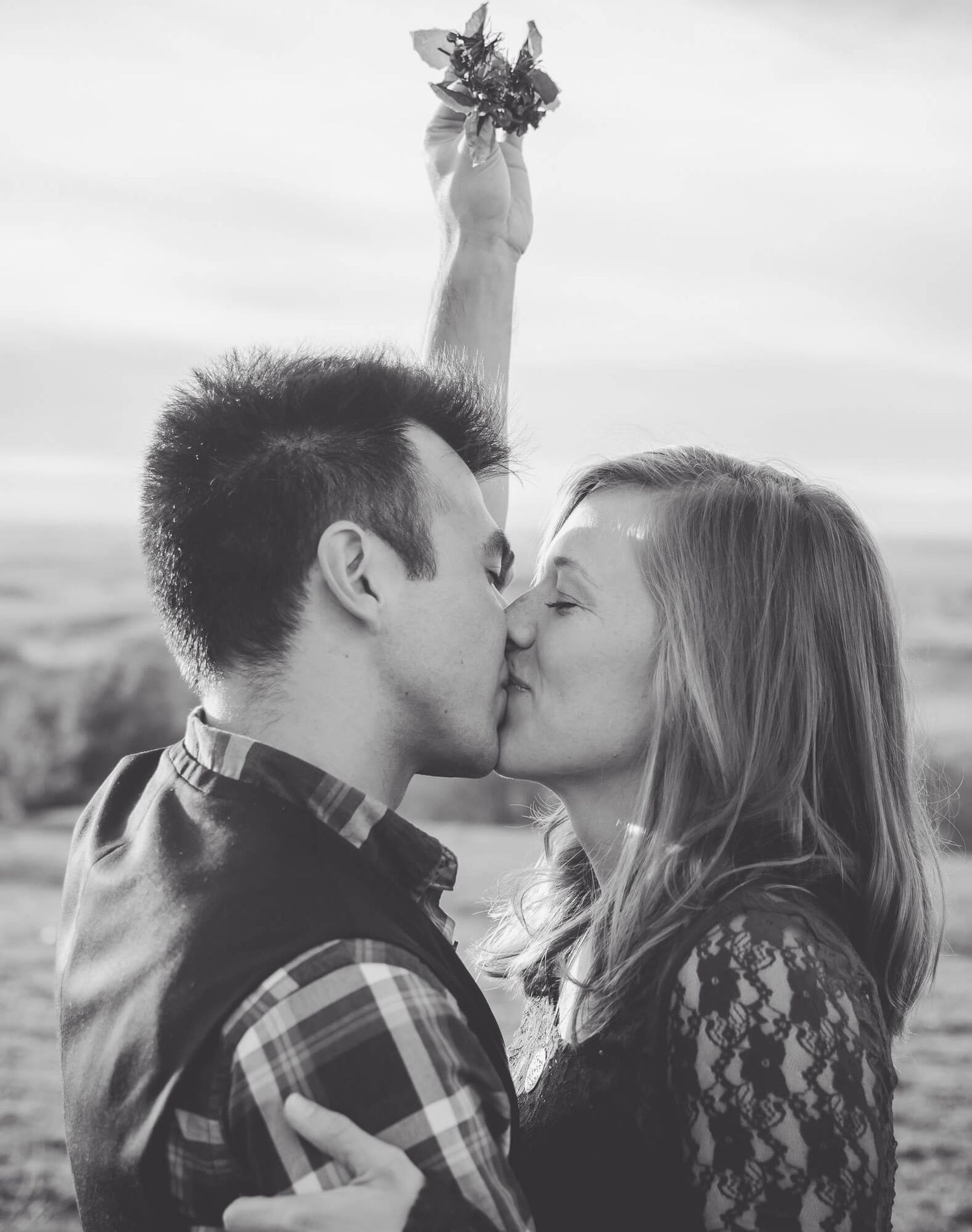 A romantic black and white photo of a couple sharing intimate kisses on a cloudy beach while having an Omaha couple's photography session.