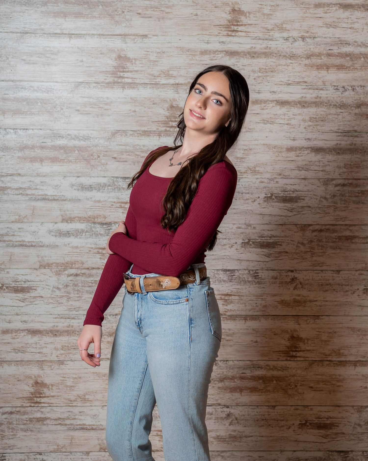 Someone demonstrates weight loss progress by holding out the waistband of loose-fitting jeans against a rustic wood background.