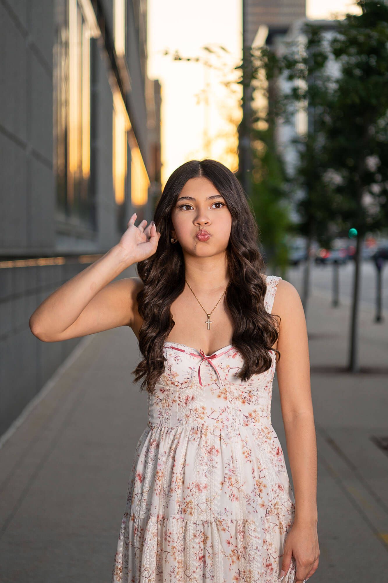 A person in a floral dress poses playfully against a city backdrop during golden hour.