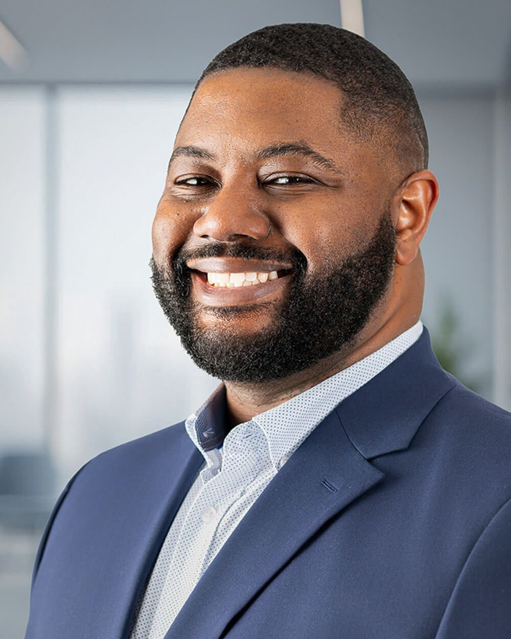 Professional headshot of a smiling person in a navy suit jacket and light blue button-down shirt.