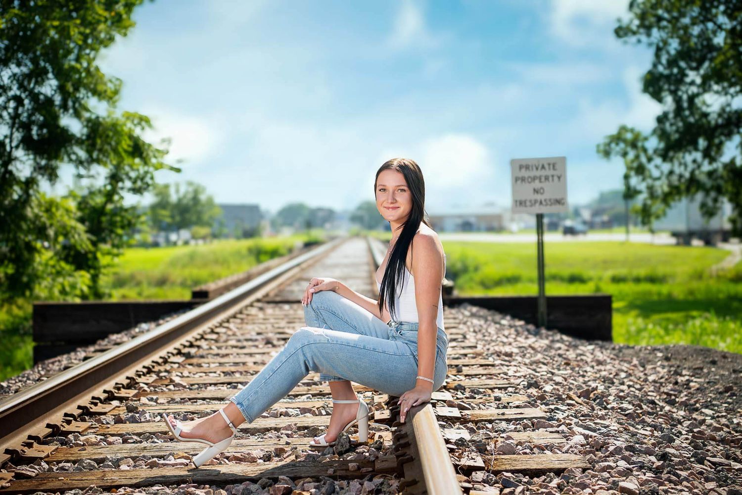 A person in a white dress sits thoughtfully on railroad tracks stretching into the distance on a sunny day.