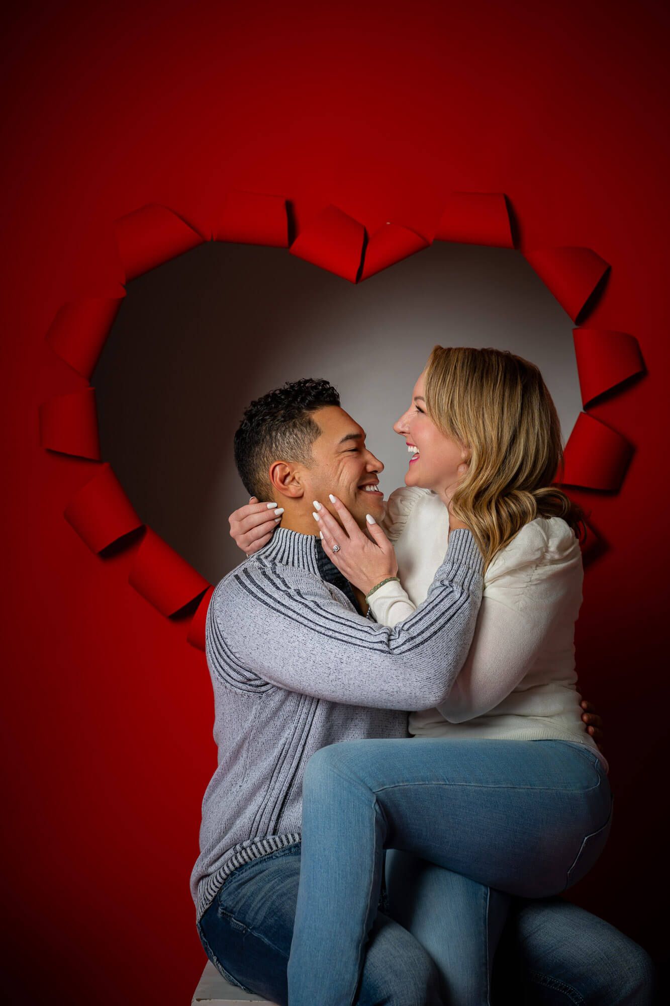 Omaha couple's photographer captures couple in gray sweaters share an intimate moment against a dramatic red and black heart shaped backdrop
