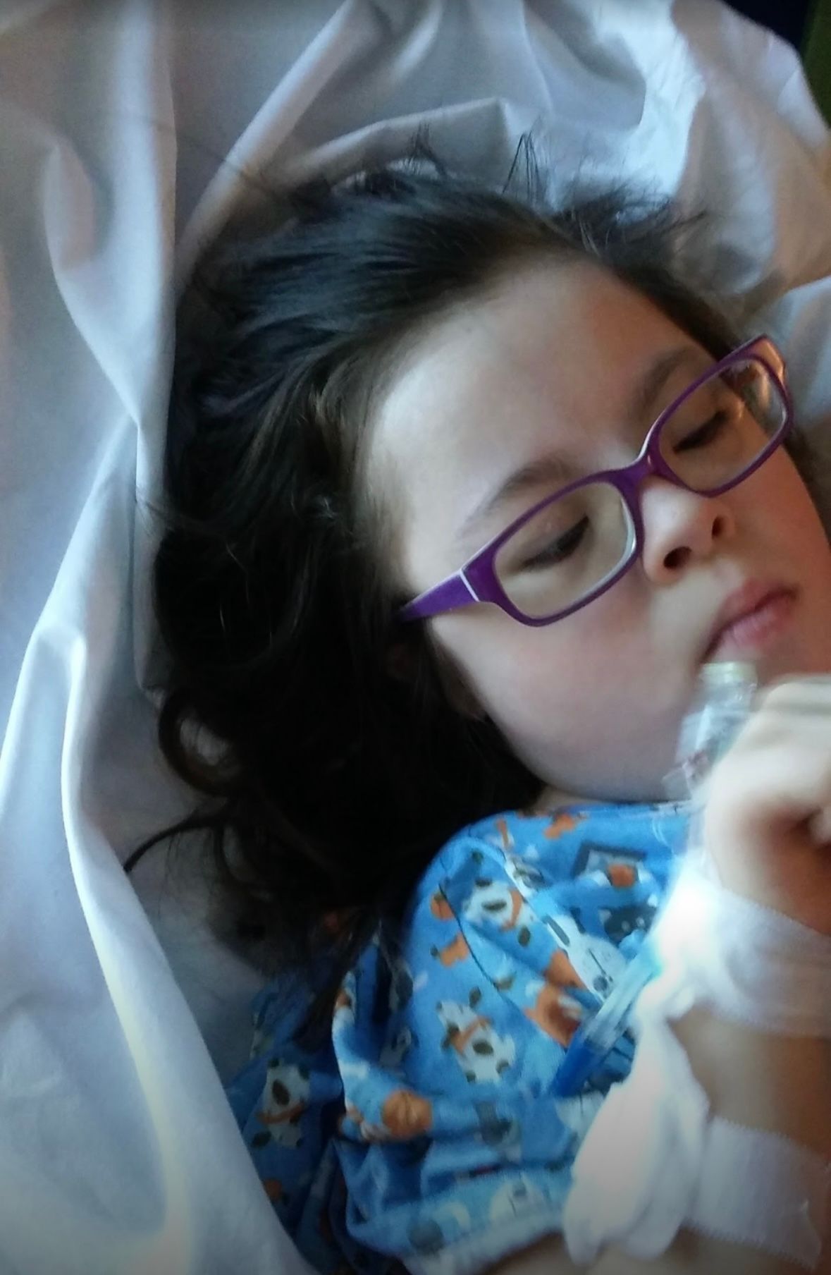 A peaceful sleeper wearing purple glasses and a blue patterned pajama top rests against white bedding.