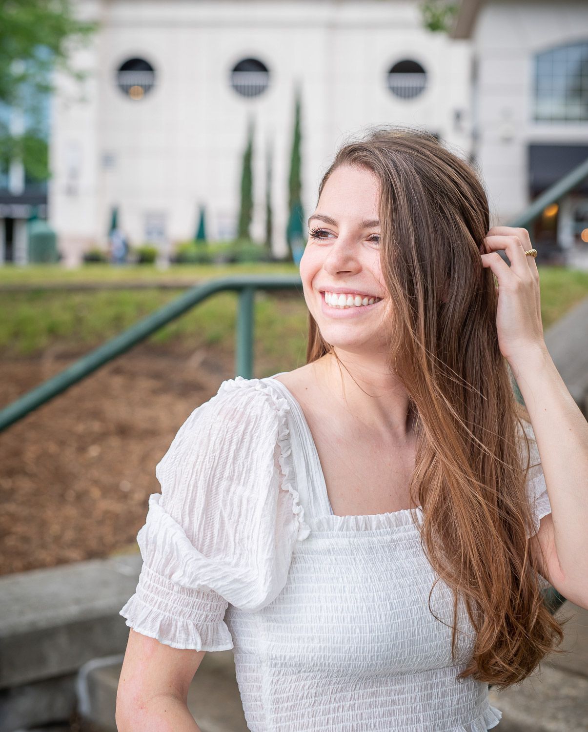 Senior photography in Omaha in a white smocked dress poses outdoors in a series of candid shots showing joyful expressions.