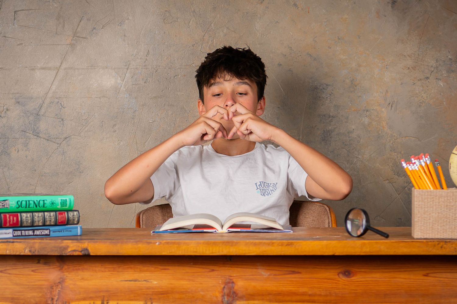 Student expressing frustration while studying at desk with books and school supplies.