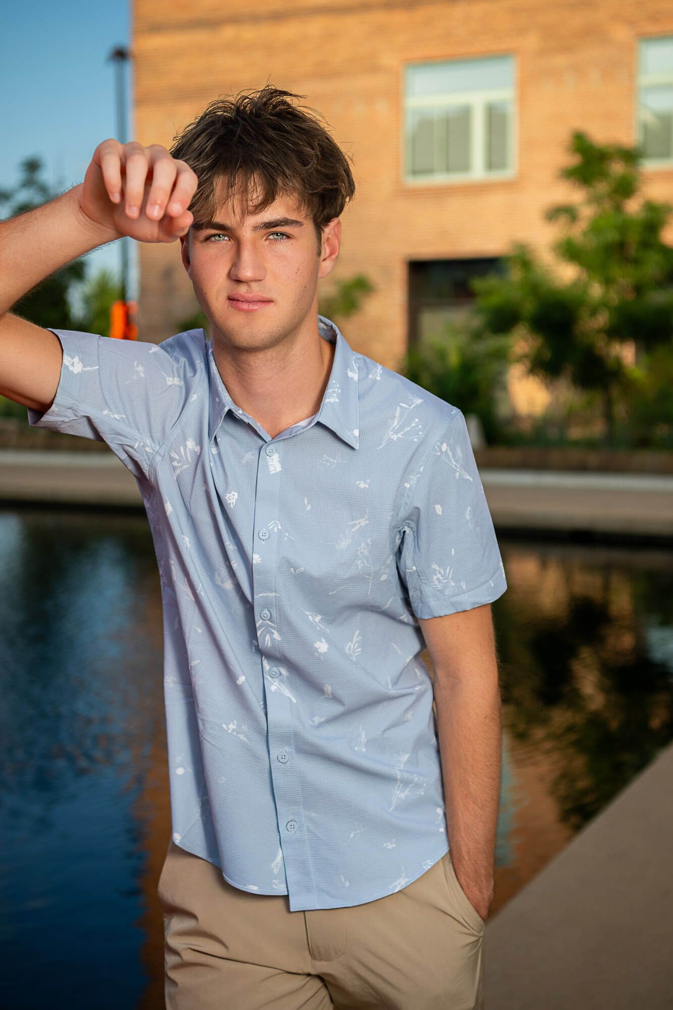 A person in a light blue button-down shirt and khaki pants poses against an outdoor backdrop at sunset.